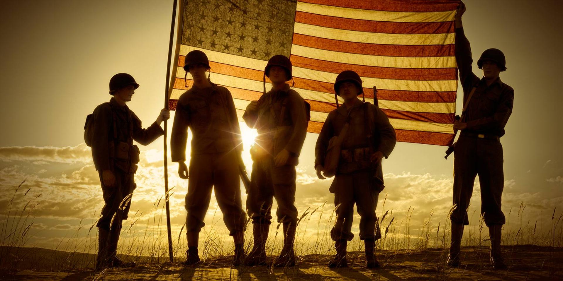 Photo of American soldiers holding up flag and silhouetted by the sun in the background